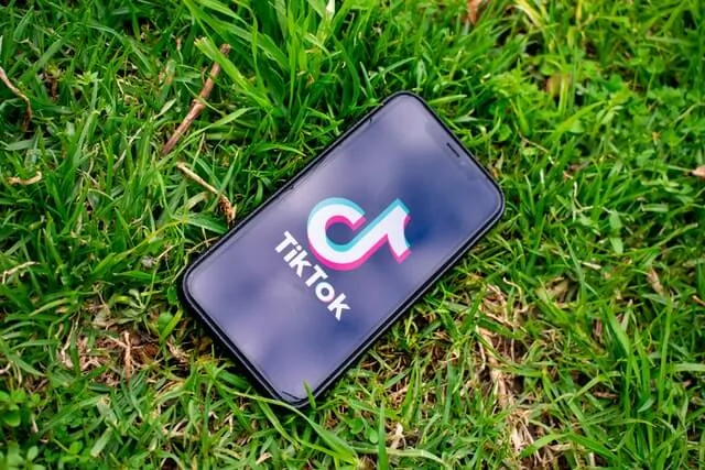 Smartphone displaying the TikTok logo lying on grass