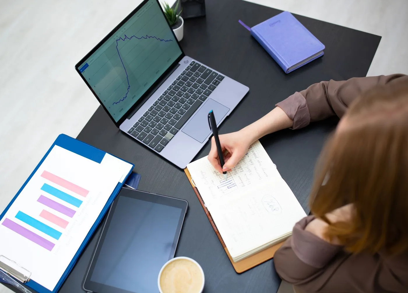 Writing a monthly SEO report beside a laptop showing performance graphs